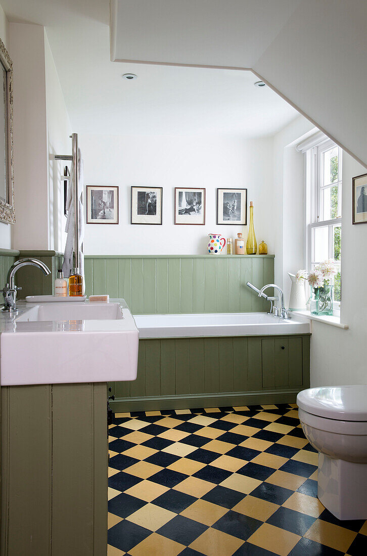 Getäfeltes grünes Bad mit kariertem Boden im Badezimmer eines Hauses in Sussex Downs, England, UK