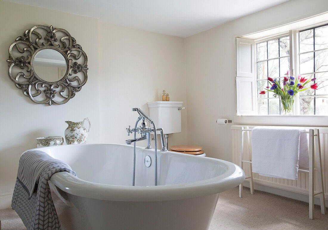 Freestanding bath with decorative mirror in bathroom with tulips in window of Burwash home East Sussex England UK