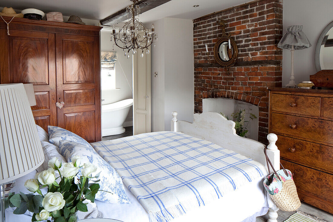 Karierte Decke auf einem Bett mit offenem Kamin in einem Schlafzimmer in West Sussex, England UK