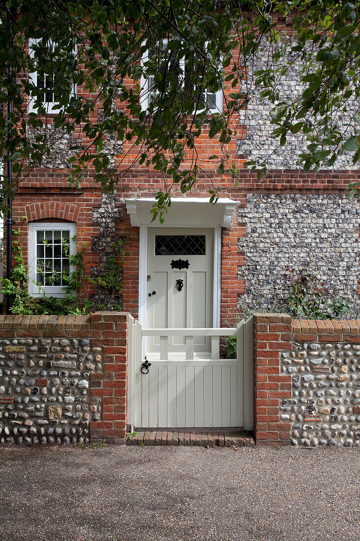 Weißes Tor mit Kieselsteinen und Backsteinfassade eines Hauses in West Sussex, England, Vereinigtes Königreich
