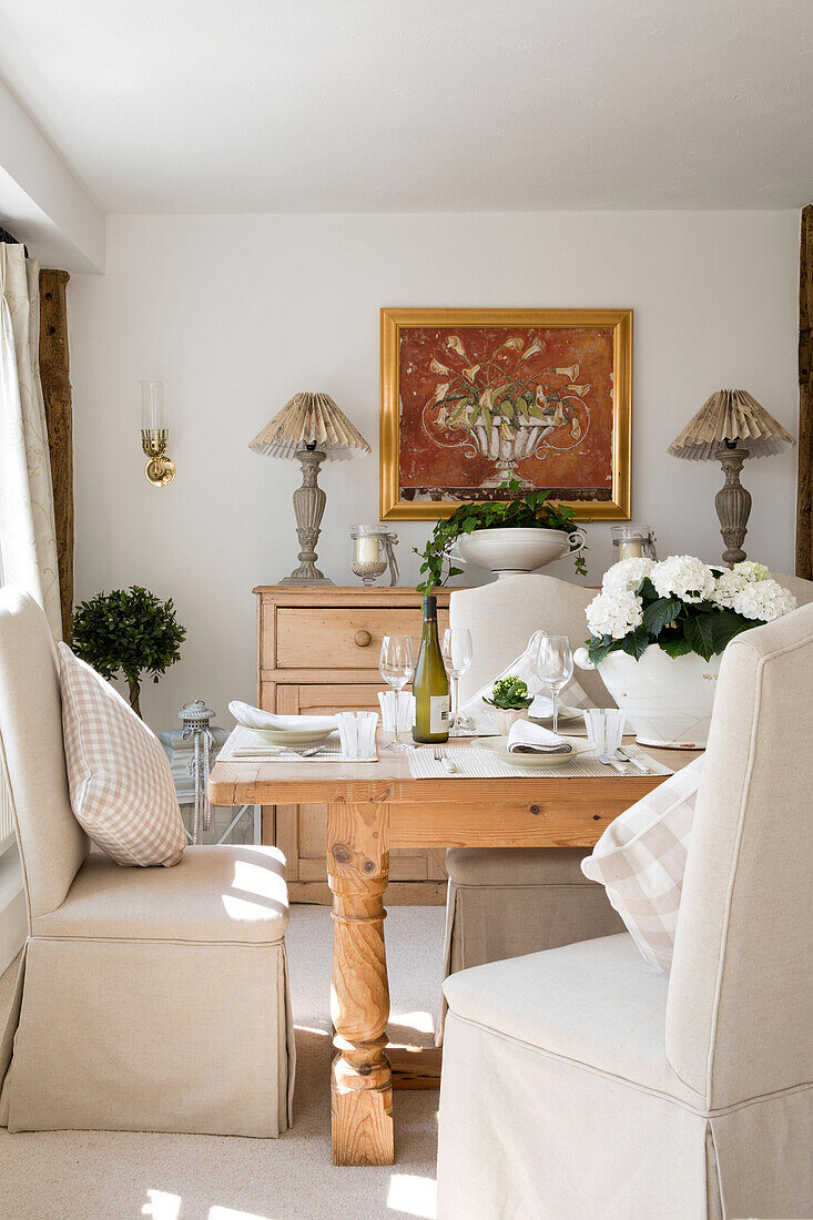 Stühle mit Schlupfbezügen am Tisch mit goldgerahmten Kunstwerken im Esszimmer in West Maling, Kent, England, UK