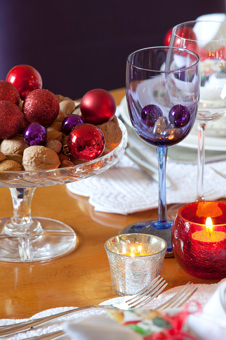 Red baubles and buts with lit candles on dining table in West Sussex home, England, UK