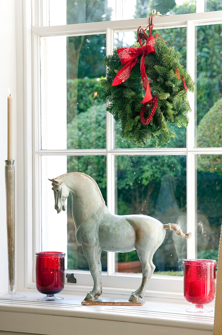 Reiterstandbild mit roten Kerzenhaltern und Weihnachtskranz auf der Fensterbank in einem Haus in West Sussex, England, Vereinigtes Königreich