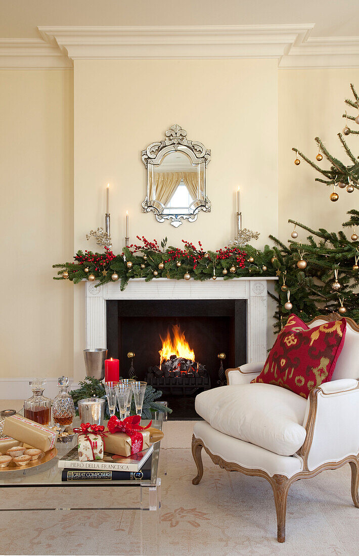 Weißer Sessel am beleuchteten Kamin mit Weihnachtsgirlande in einem Haus in West Sussex, England, UK