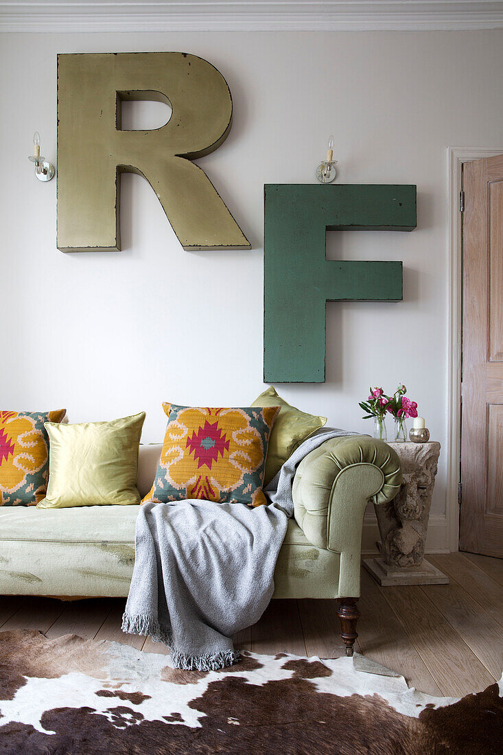An der Wand montierte Buchstaben R und F über einem Sofa mit Knöpfen im Wohnzimmer eines Londoner Stadthauses, England, UK