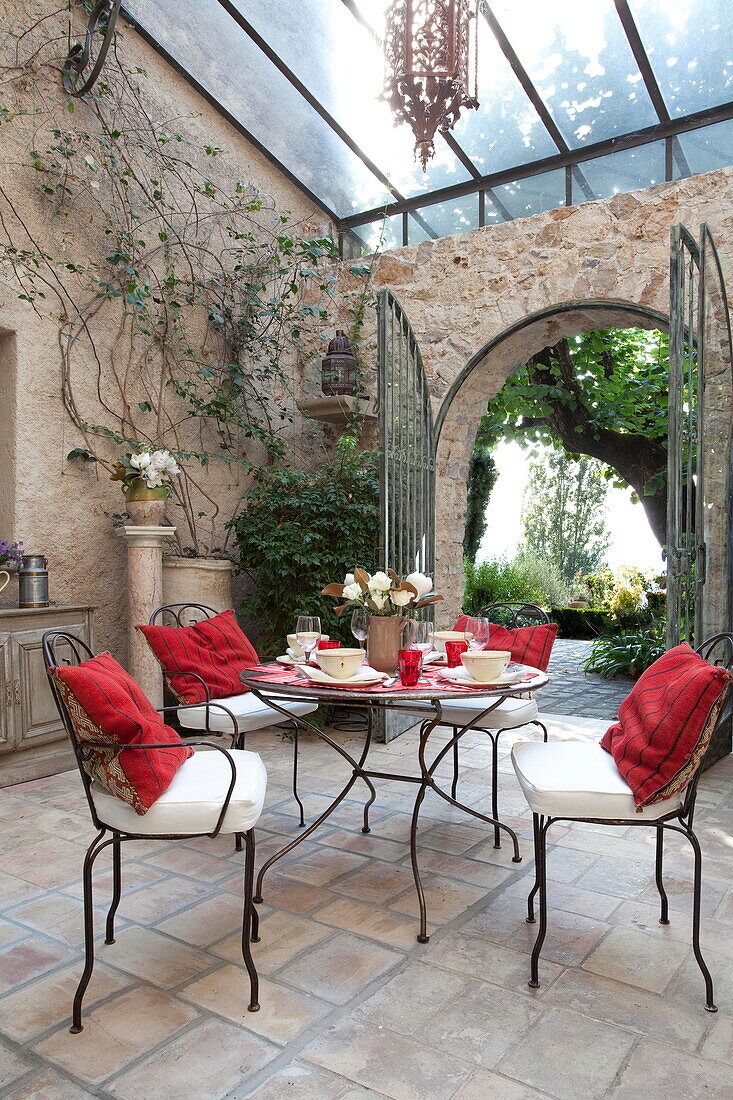 Red cushions on metal chairs in dining room conservatory of French holiday villa