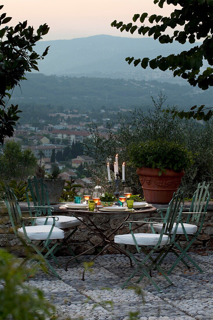 Kerzen auf einem Tisch mit Stühlen in der Abenddämmerung mit Blick aus einer französischen Ferienvilla