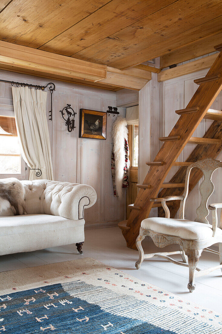 Sofa und Sessel mit Holztreppe im Wohnzimmer eines Bergchalets in Chateau-d'Oex, Waadt, Schweiz