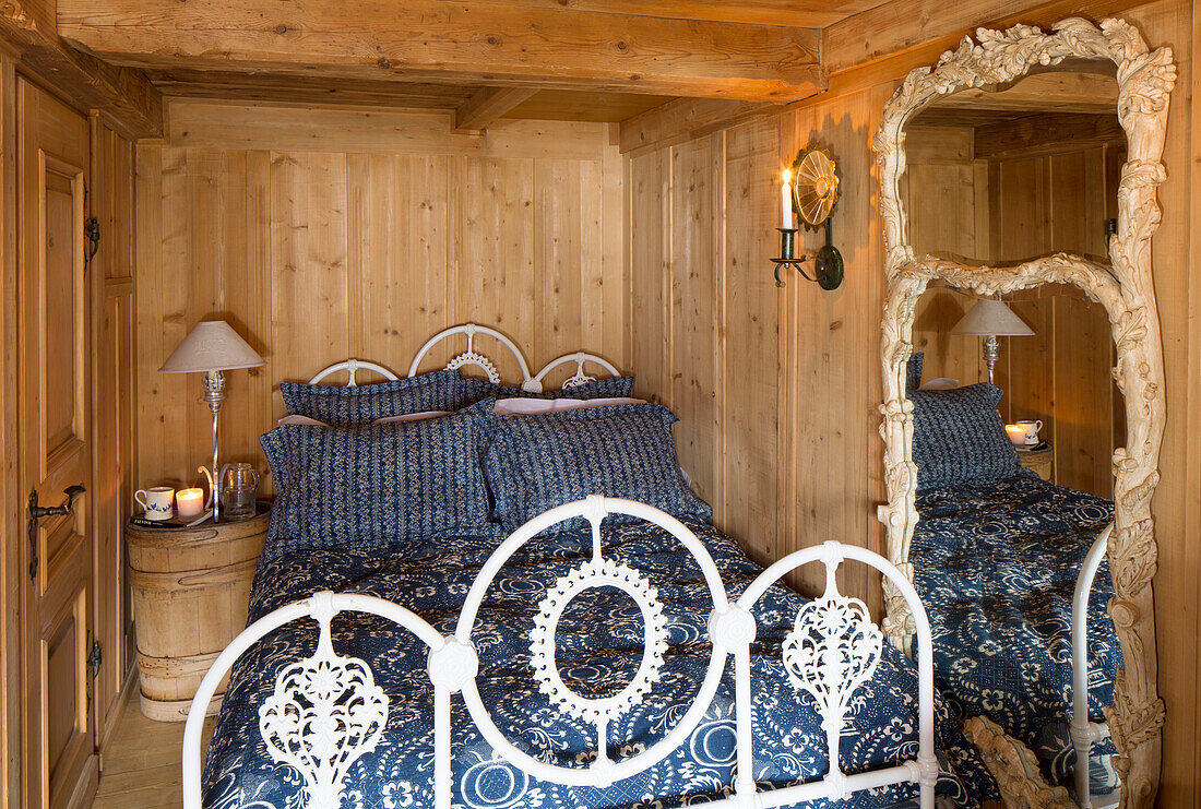 Weißes schmiedeeisernes Bett in einem holzgetäfelten Zimmer eines Bergchalets in Chateau-d'Oex, Waadt, Schweiz