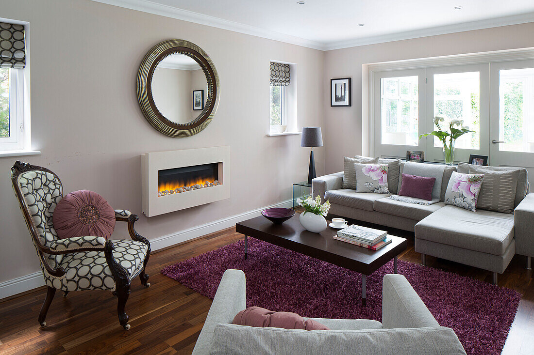 Runder Spiegel mit Ecksofa im pastellrosa Wohnzimmer eines Familienhauses in London, England, Vereinigtes Königreich
