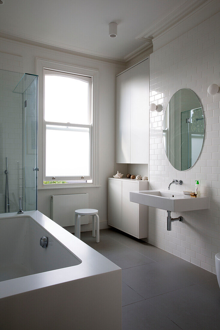 Runder Spiegel über dem Waschbecken in einem weiß gefliesten Badezimmer in einem Haus in Oxfordshire, England, UK