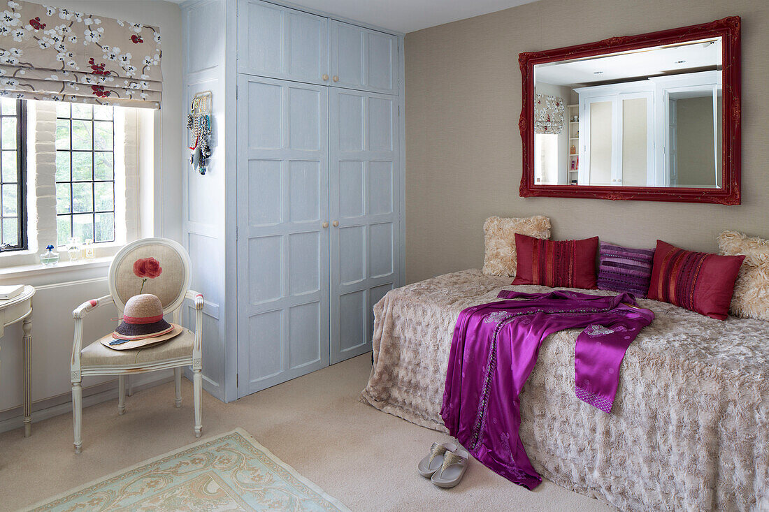 Red painted mirror frame above single bed with light blue painted wardrobe in bedroom of London home, UK