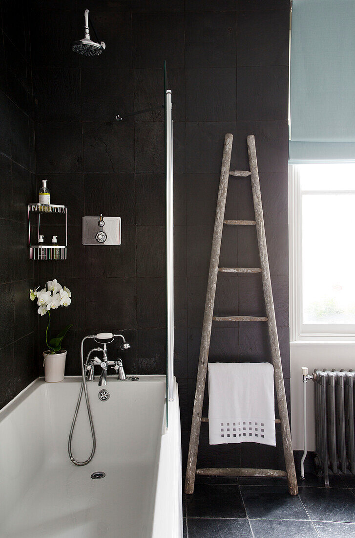 Ladder with towel at window with shower screen in black tiled bathroom of London townhouse England UK