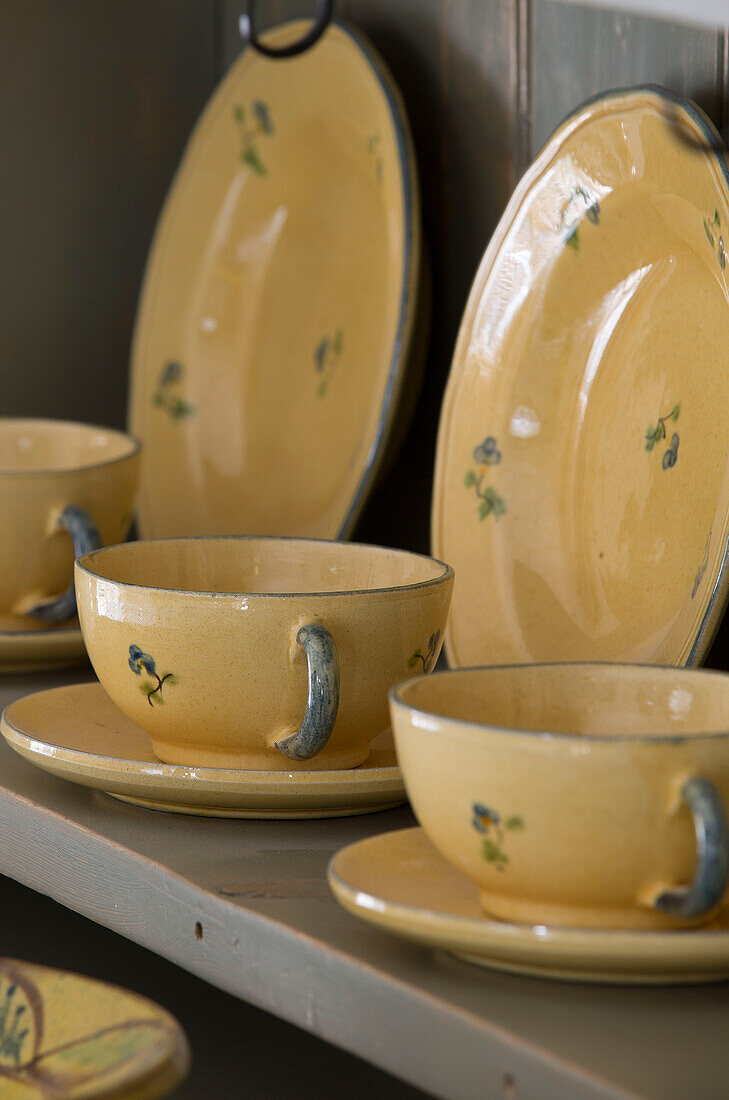 Gelbe Tassen und Untertassen mit Tellern auf der Küchenkommode eines britischen BauernhausesUK