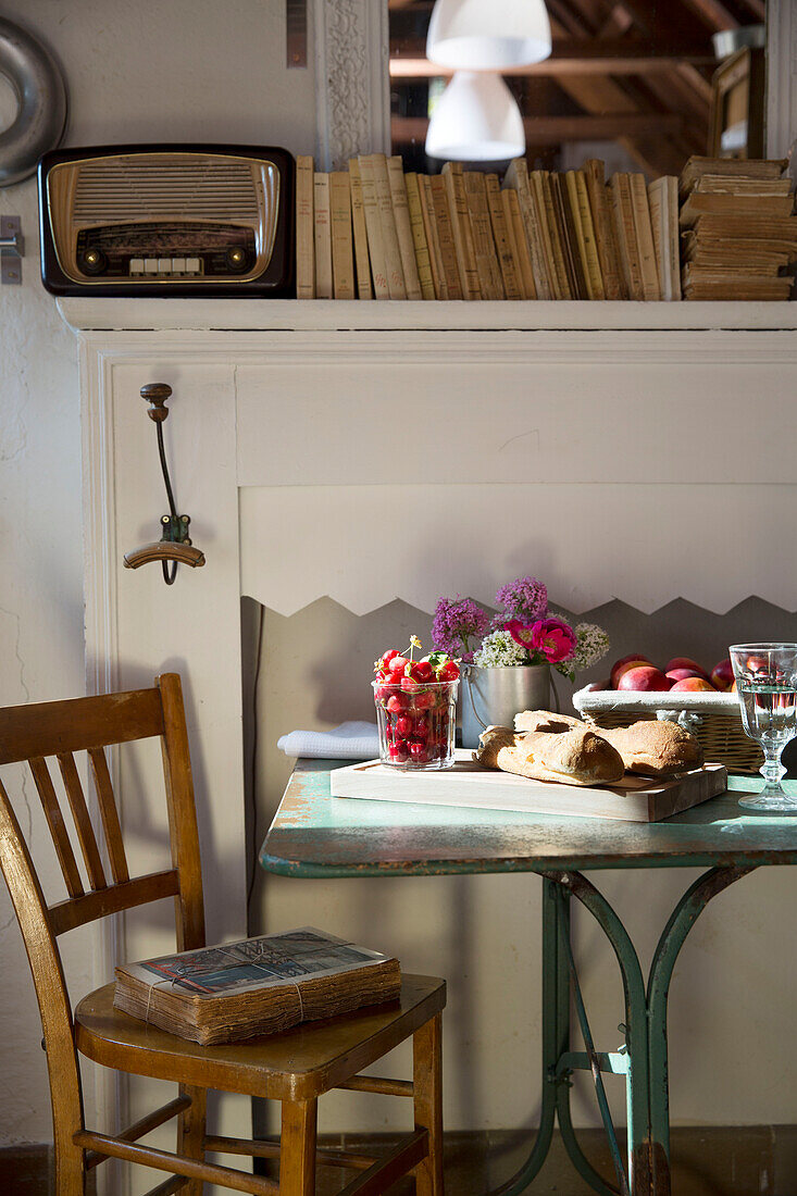 Obst und Brot auf einem sonnenbeschienenen Tisch mit Büchern und Radio auf dem Kaminsims in einer französischen Bauernhausküche