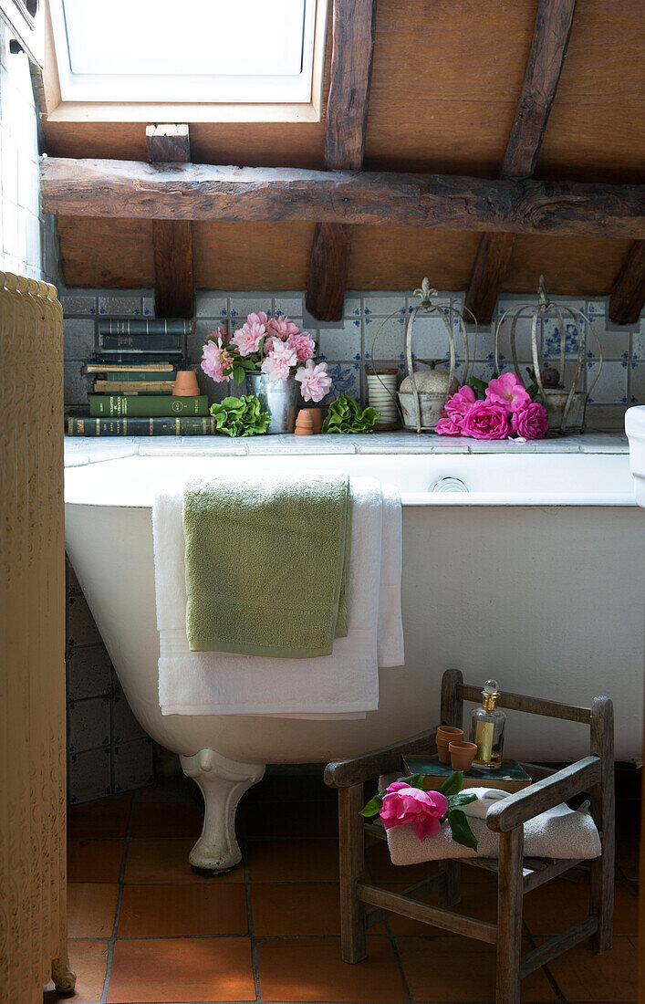 Gefaltete Handtücher mit Büchern und Schnittblumen neben der Badewanne in einem französischen Cottage