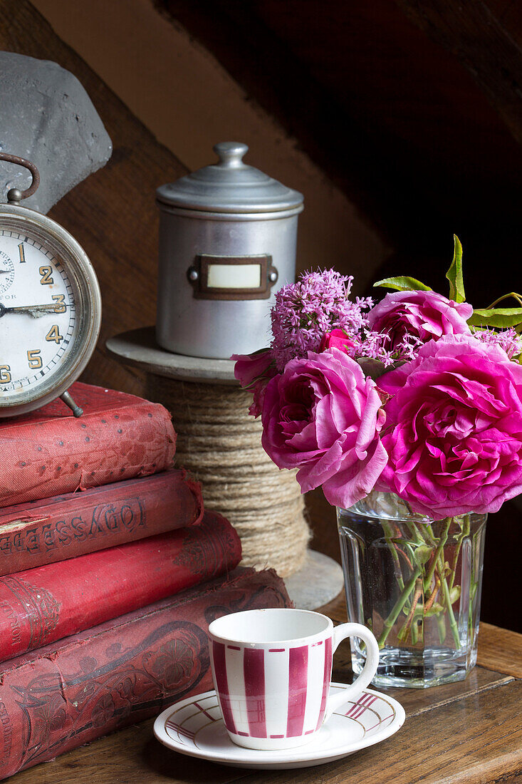 Rosa Rosen mit Büchern mit festem Einband und einer Seilrolle in einem französischen Bauernhaus