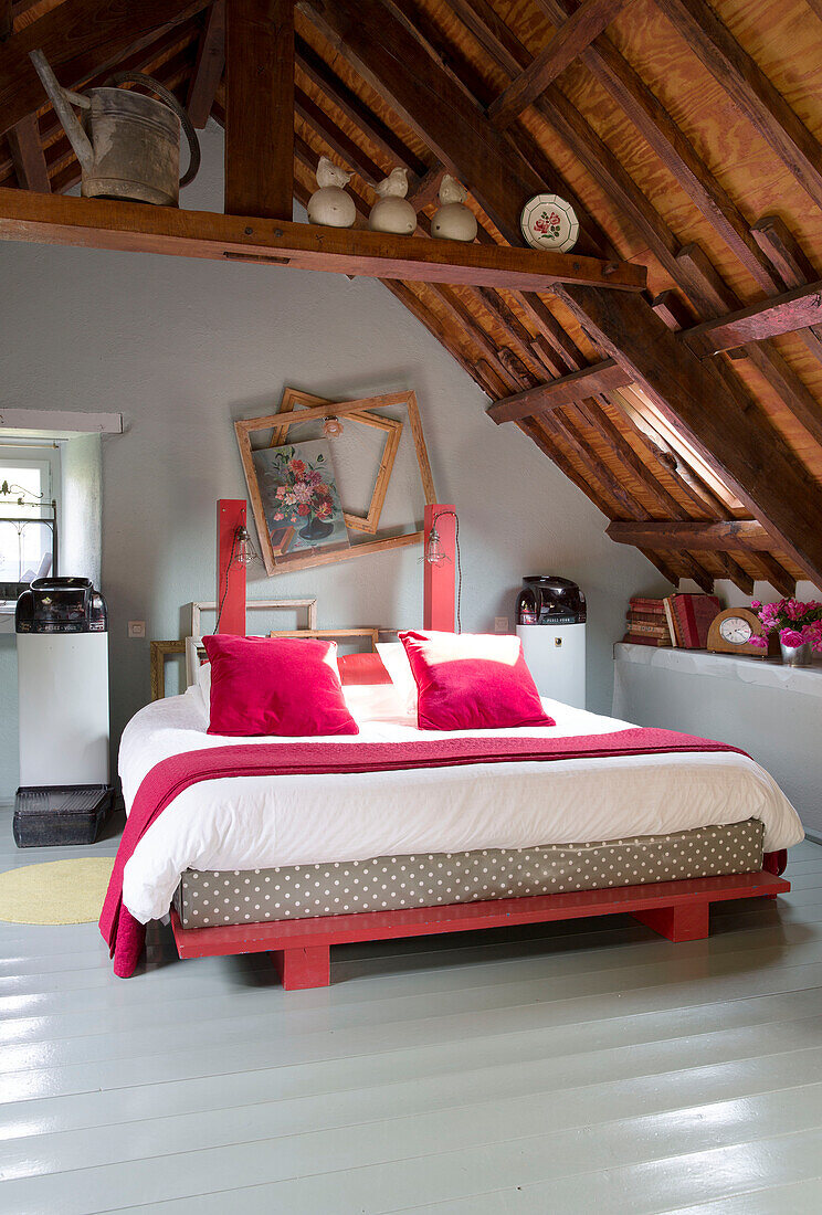 Double bed with picture frames below wooden ceiling in French farmhouse
