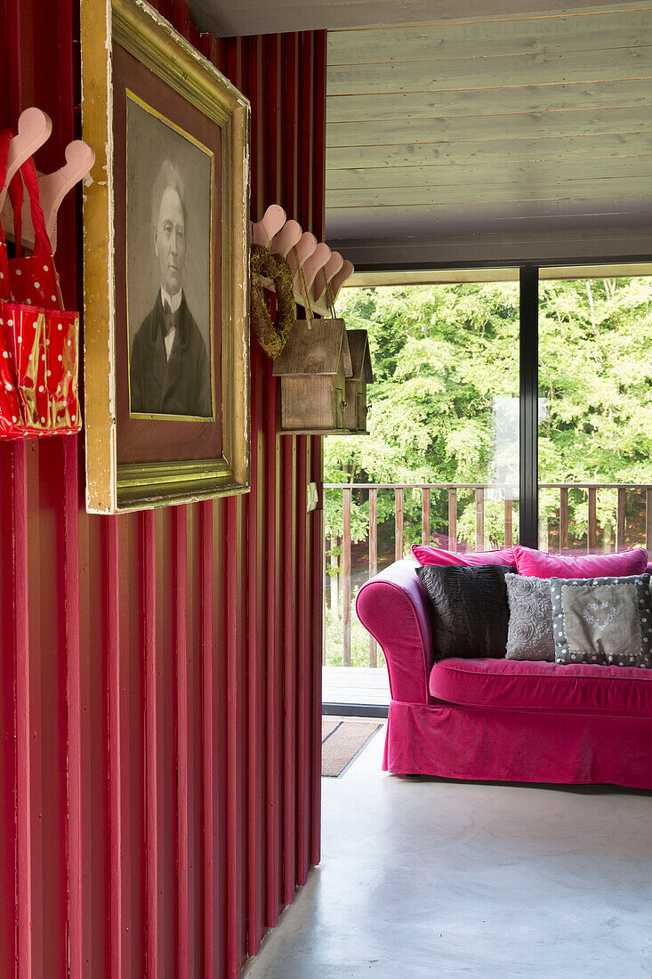 Gerahmter Druck und Kleiderhaken mit rosafarbenem Sofa in einem bretonischen Landhaus, Frankreich