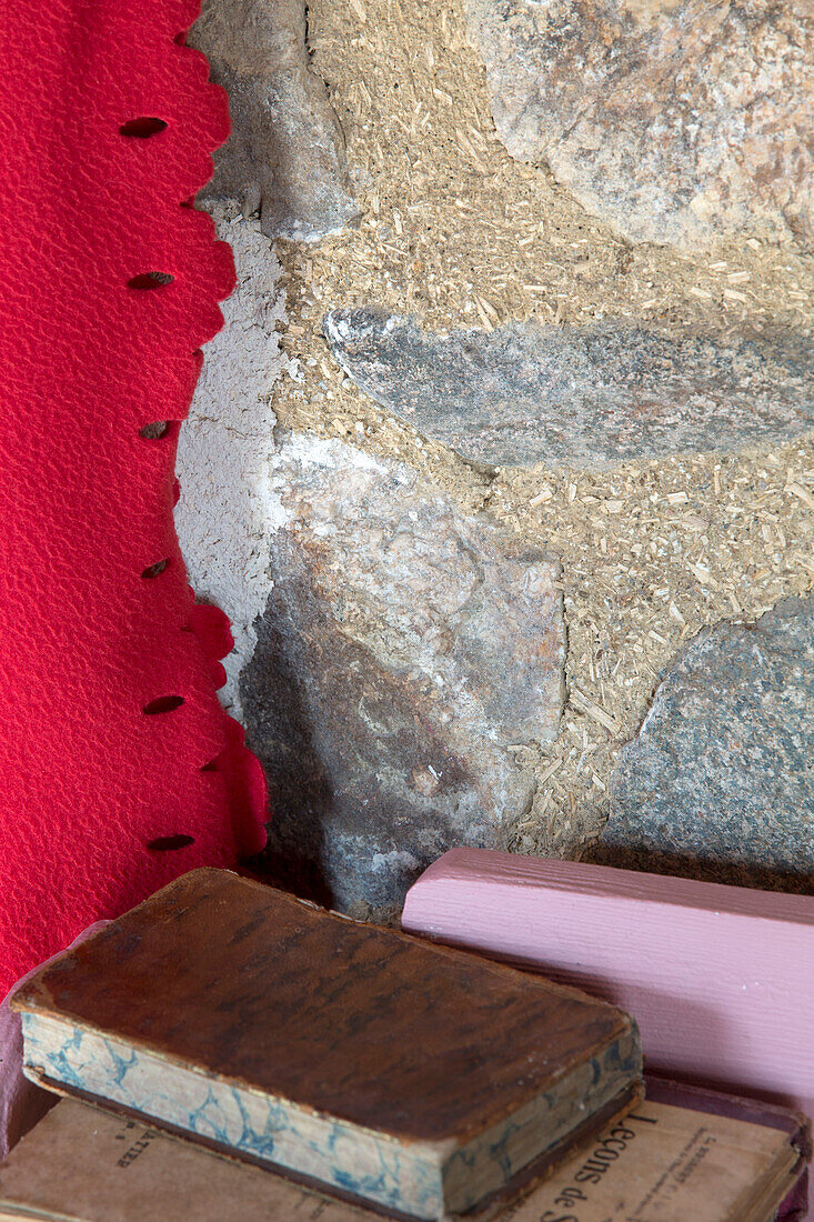 Hardbacked vintage books with red fabric and exposed stone wall in Brittany cottage, France