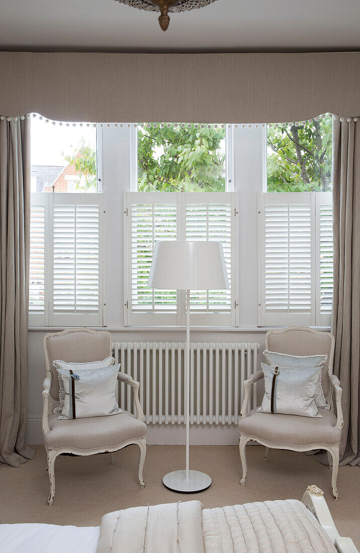 Weiße Fensterläden im Fenster mit Stehlampe und passenden Sesseln in einem Haus in Hertfordshire, England, UK