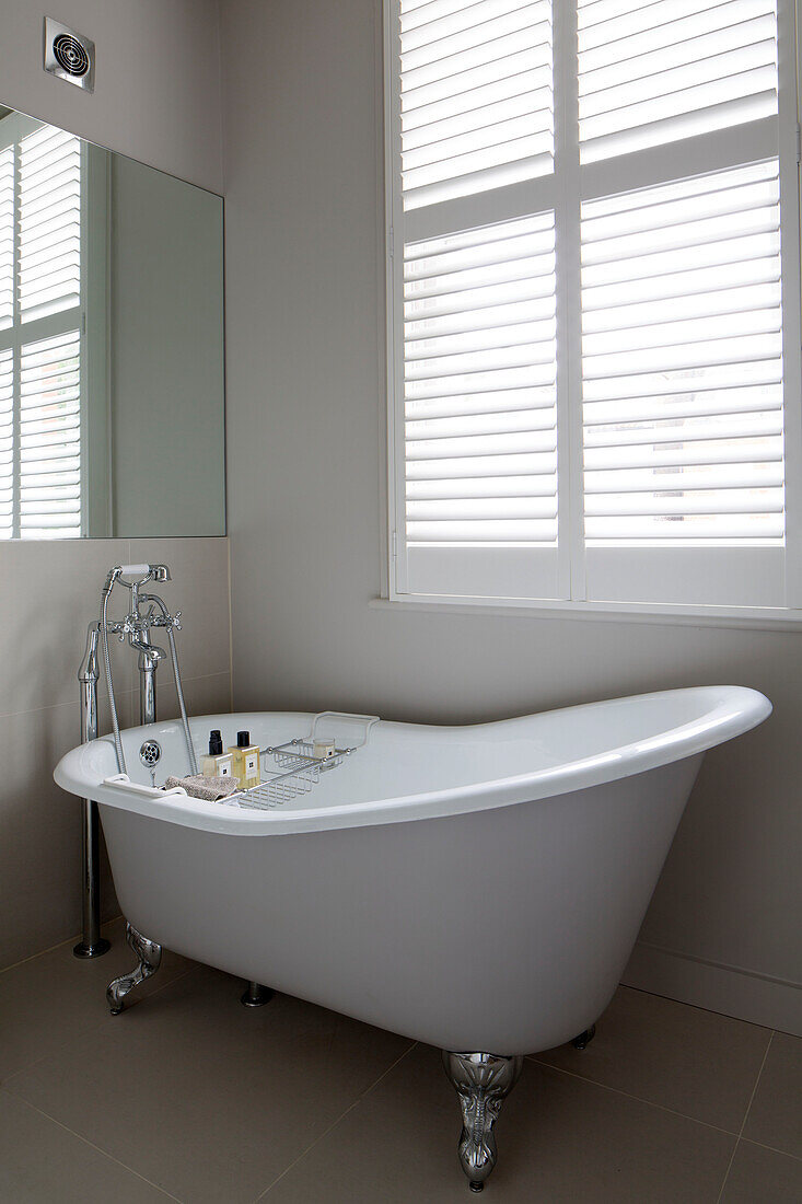 Slipper bath below shuttered window with mirror in Hertfordshire home,  England,  UK