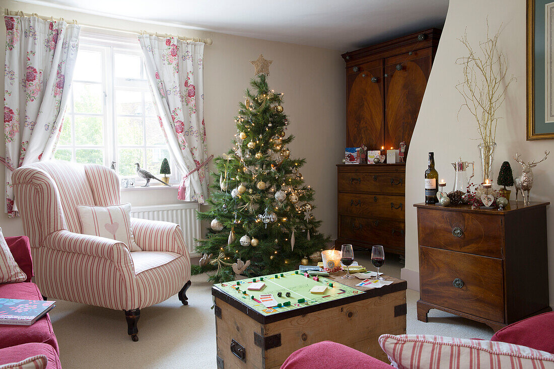 Gestreifter Sessel am Fenster des Wohnzimmers in Berkshire mit Weihnachtsbaum und Brettspiel, England, UK