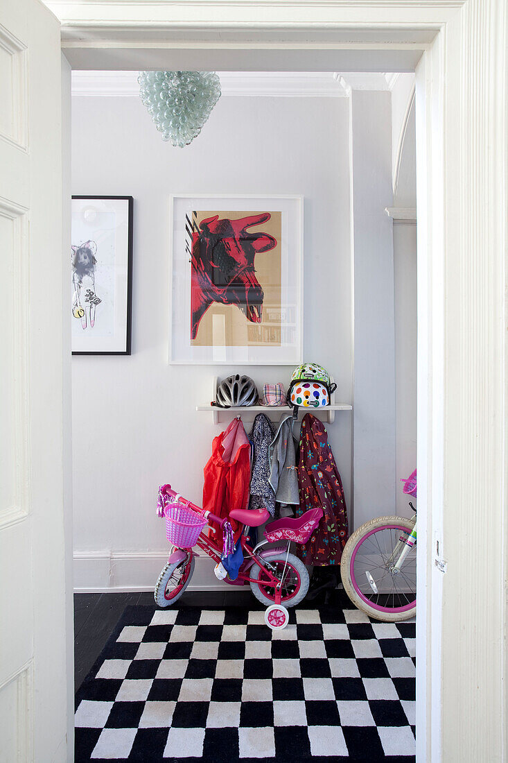 Kinderfahrräder und Fahrradhelme im Flur eines Londoner Stadthauses mit schwarz-weißem Karoteppich, England, UK