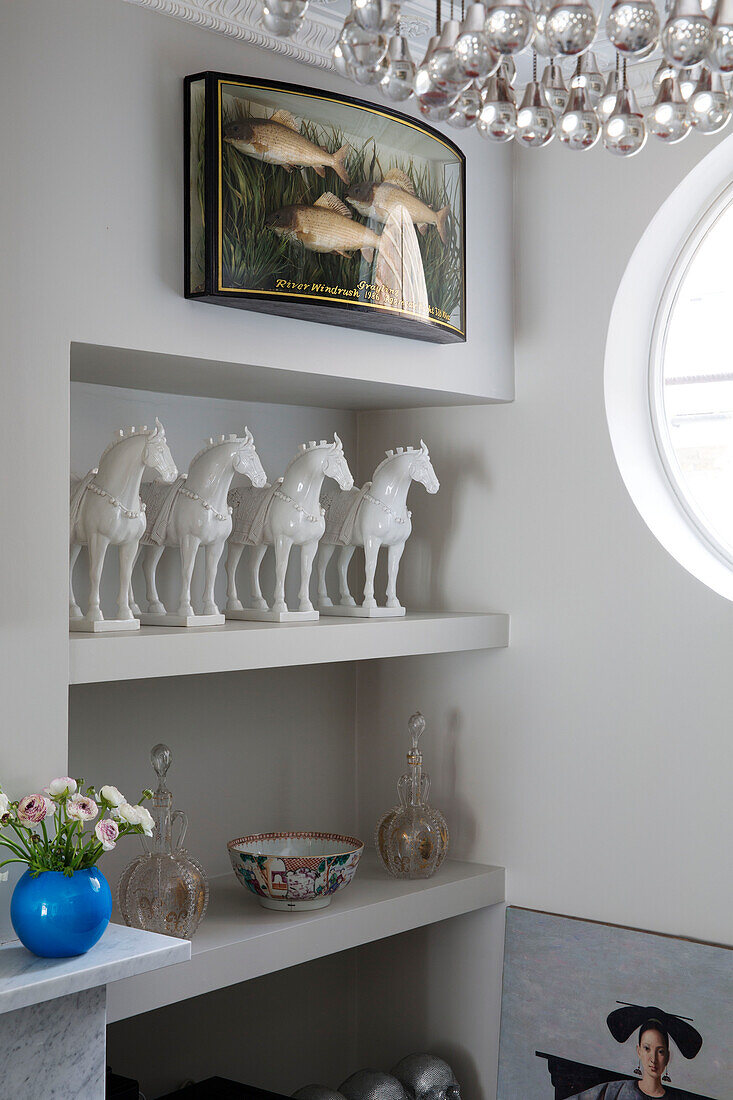 Four ceramic horses with fish in display case on white recessed shelving in London home, England, UK
