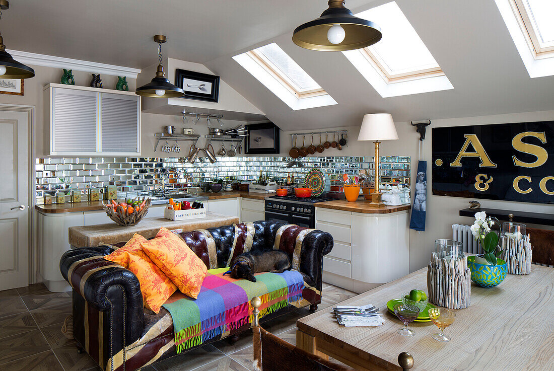 Chesterfield-Sofa unter Dachfenster in offener Dachgeschossküche mit verspiegelter Rückwand in einem Haus in London, England, UK