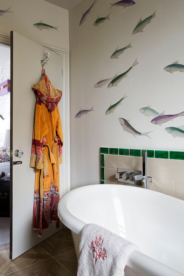 Bathrobe hangs on back door in bathroom with fish motif and freestanding bath, London home, England, UK