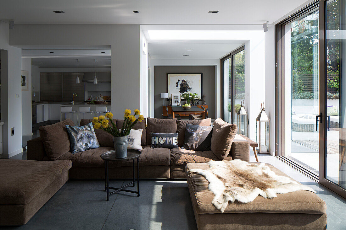Sonnendurchflutetes offenes Wohnzimmer mit braunem Sofa und Tierfellteppich in einem modernen Haus in Sussex, England, Vereinigtes Königreich