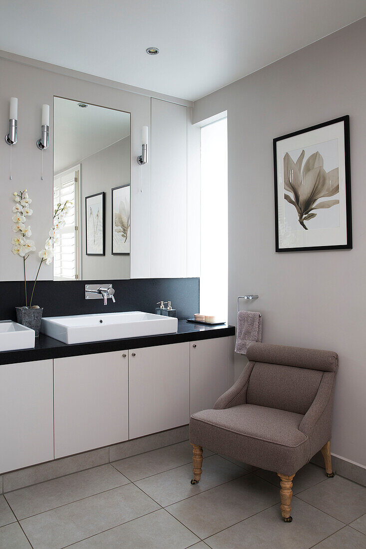 Sessel mit Kunstwerk neben einem Waschbecken mit Spiegel in einem modernen Haus in Sussex, England, UK
