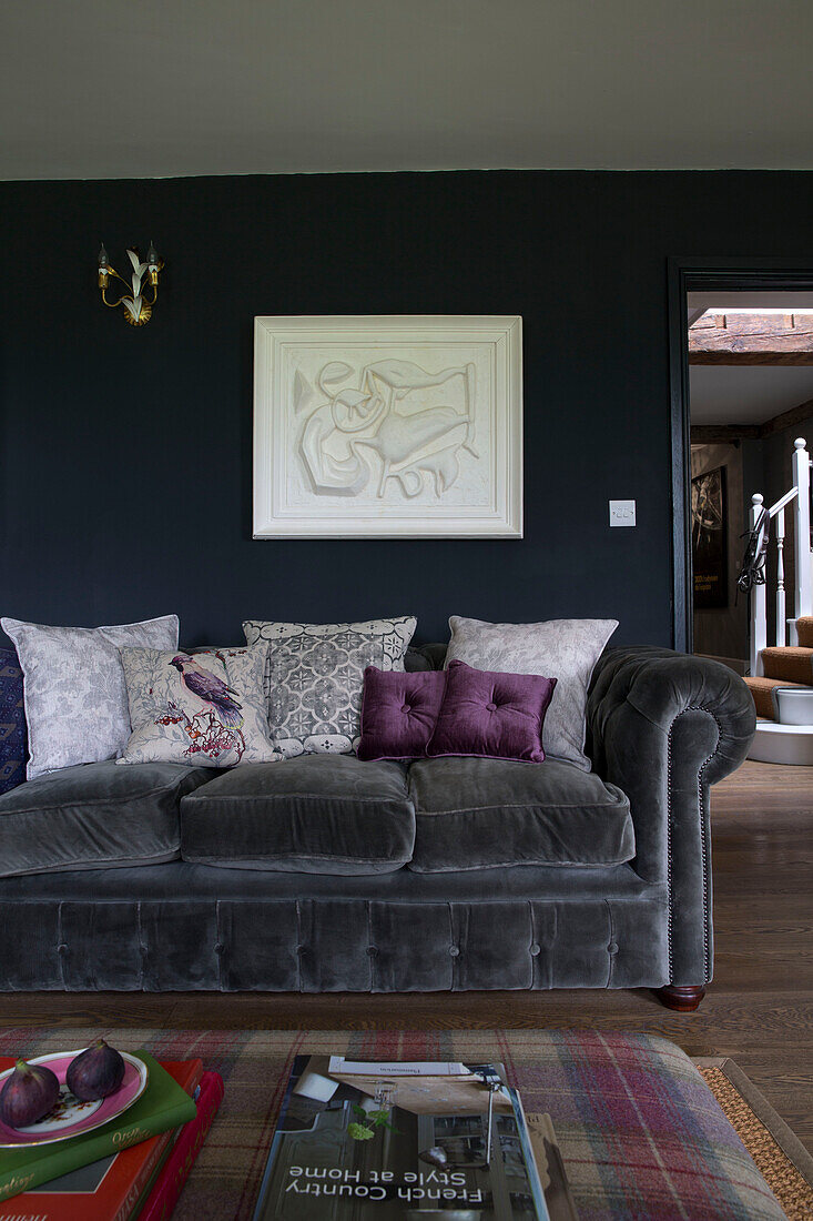 Cushions on grey velvet sofa below relief carving in Sussex home UK