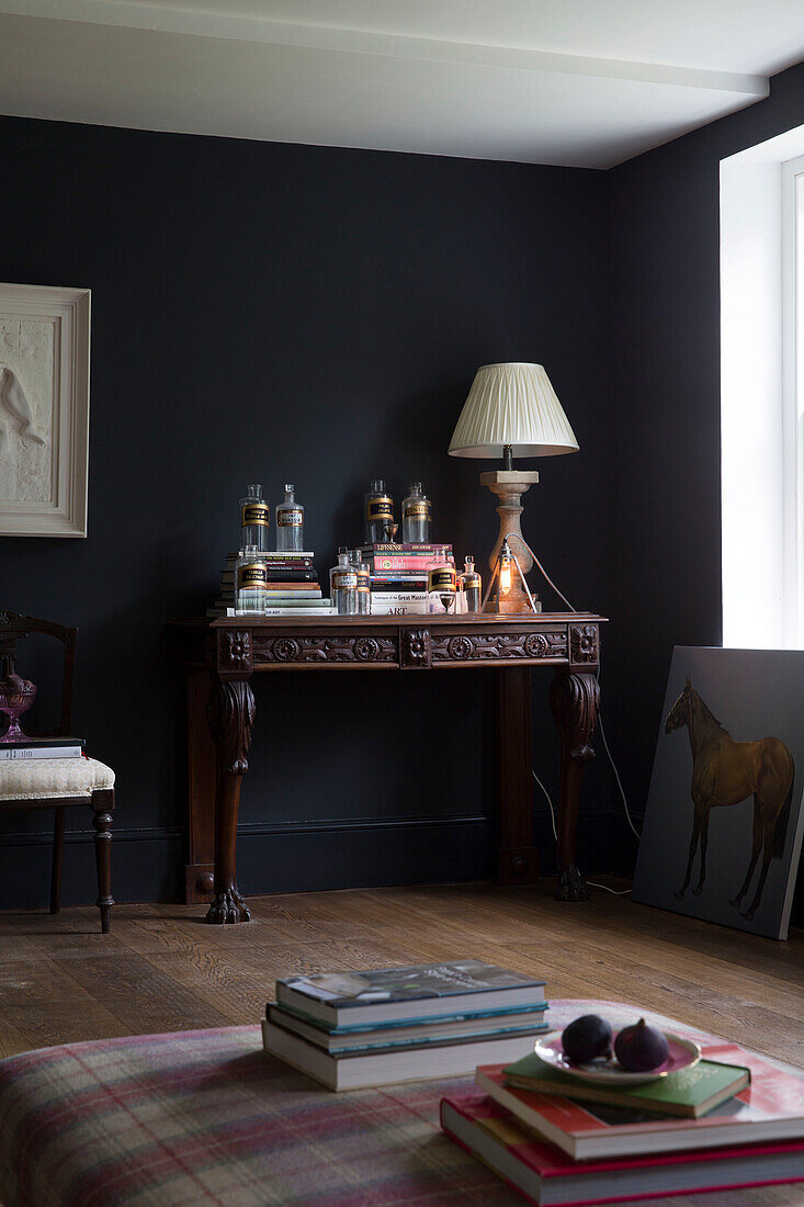 Lampe und Bücher auf geschnitztem Holztisch mit Feigen auf Ottomane im Wohnzimmer in Sussex, UK