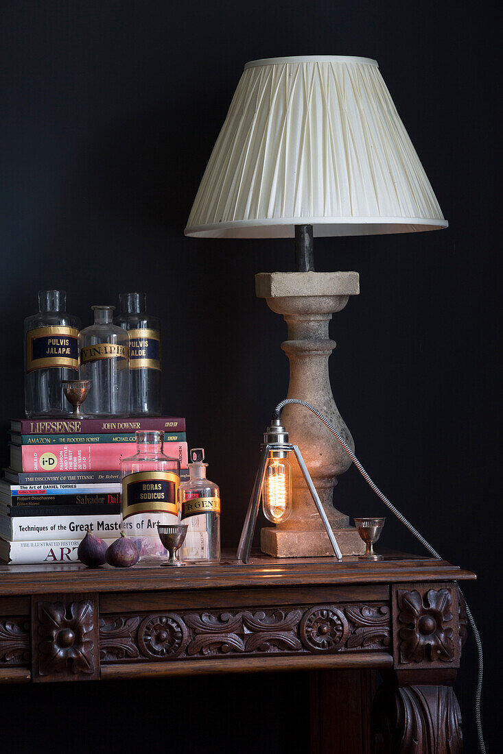 White lamp with medicine bottles with books on carved wooden table in Sussex home UK