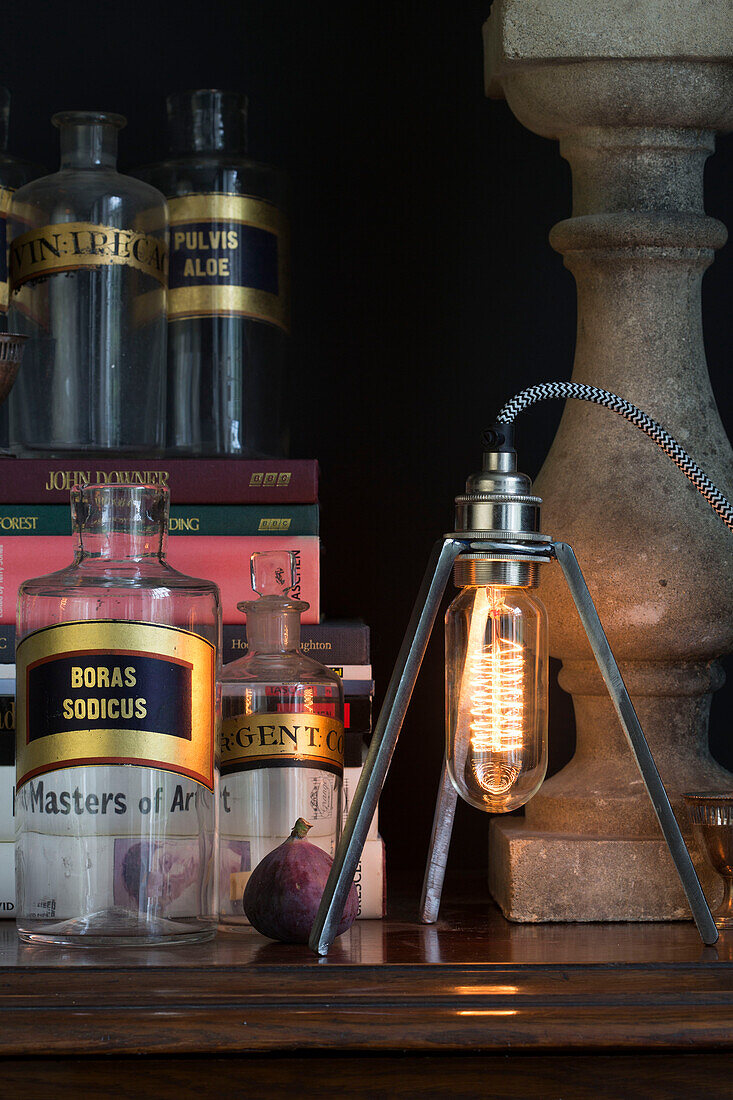 Modern light fitting with vintage medicine bottles and fig on wooden side table in Sussex home UK