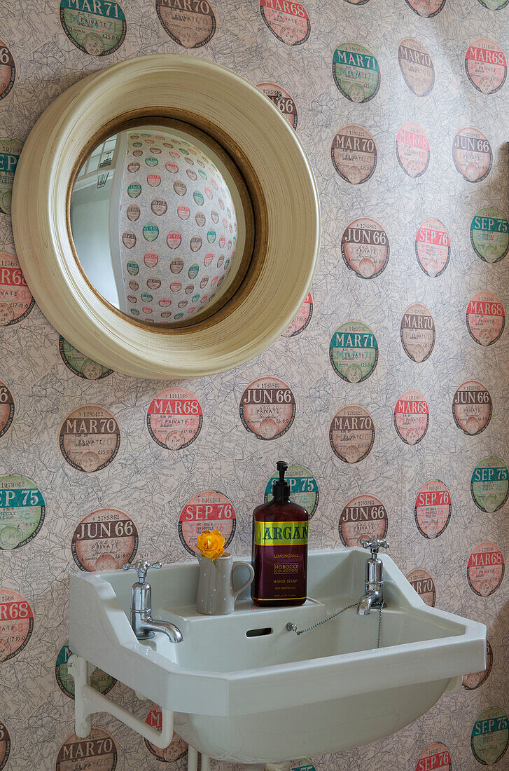 Konvexer Spiegel über dem Waschbecken mit gemusterter Weinetikettentapete in einem Haus in Surrey, England, UK