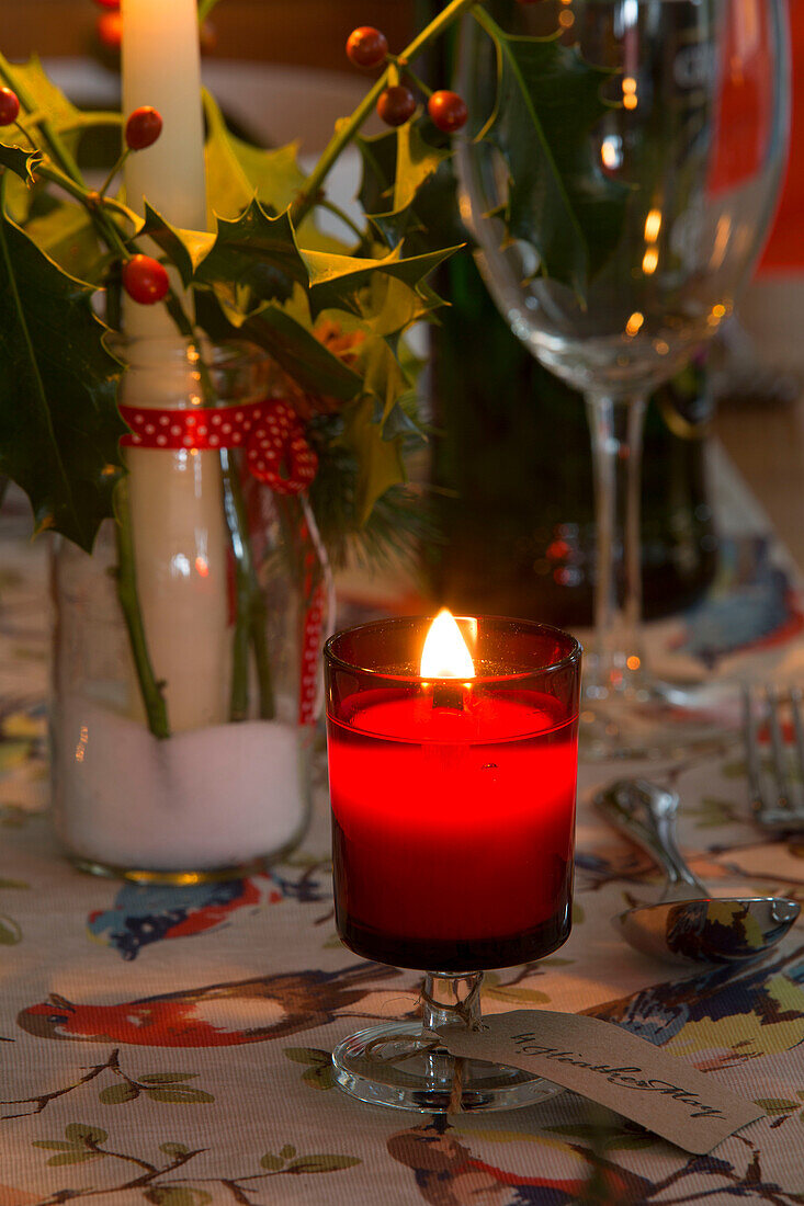 Beleuchtete Kerze in rotem Glas mit Stechpalme auf dem Esstisch in Dronfield home Derbyshire England UK