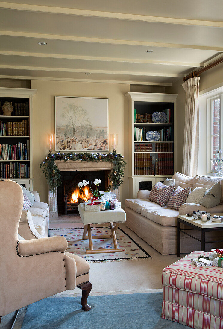Beleuchtetes Feuer mit Weihnachtsgirlande und Bücherregalen im Wohnzimmer von Lymington Hampshire UK