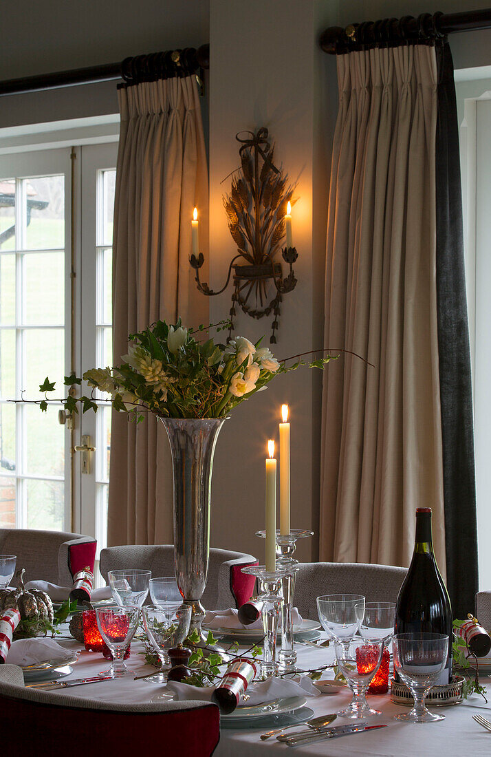 Lit candles with white roses in silver vase on dining table at Christmas in Lymington home  Hampshire  UK