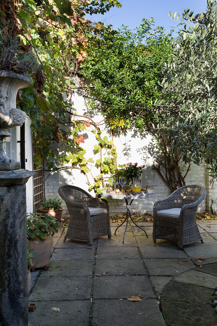Wicker armchairs in sunlit paved courtyard of Berkshire garden,  England,  UK