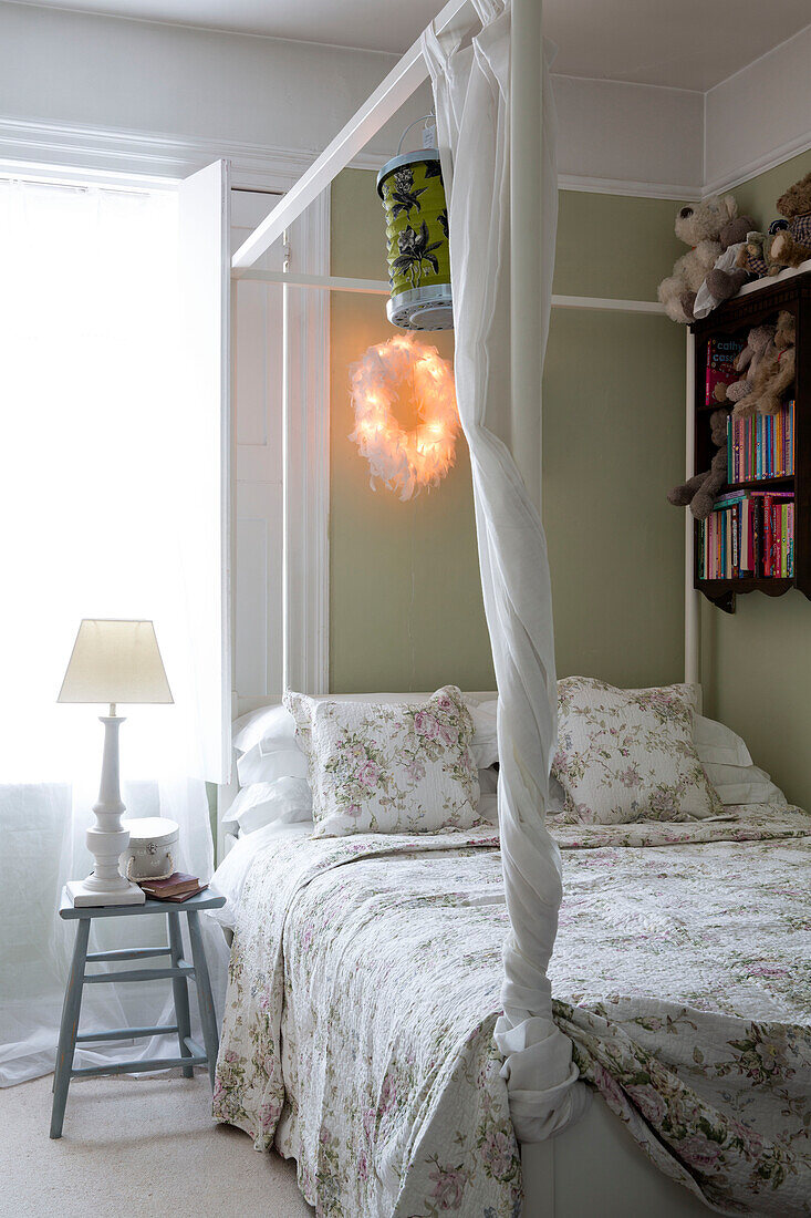 Floraler Bezug auf Himmelbett mit Bücherregal und Kuscheltieren in Haus in Berkshire, England, UK