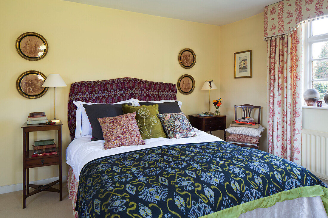 Patterned bedspread and headboard with historic artworks in bedroom of London home,  England,  UK
