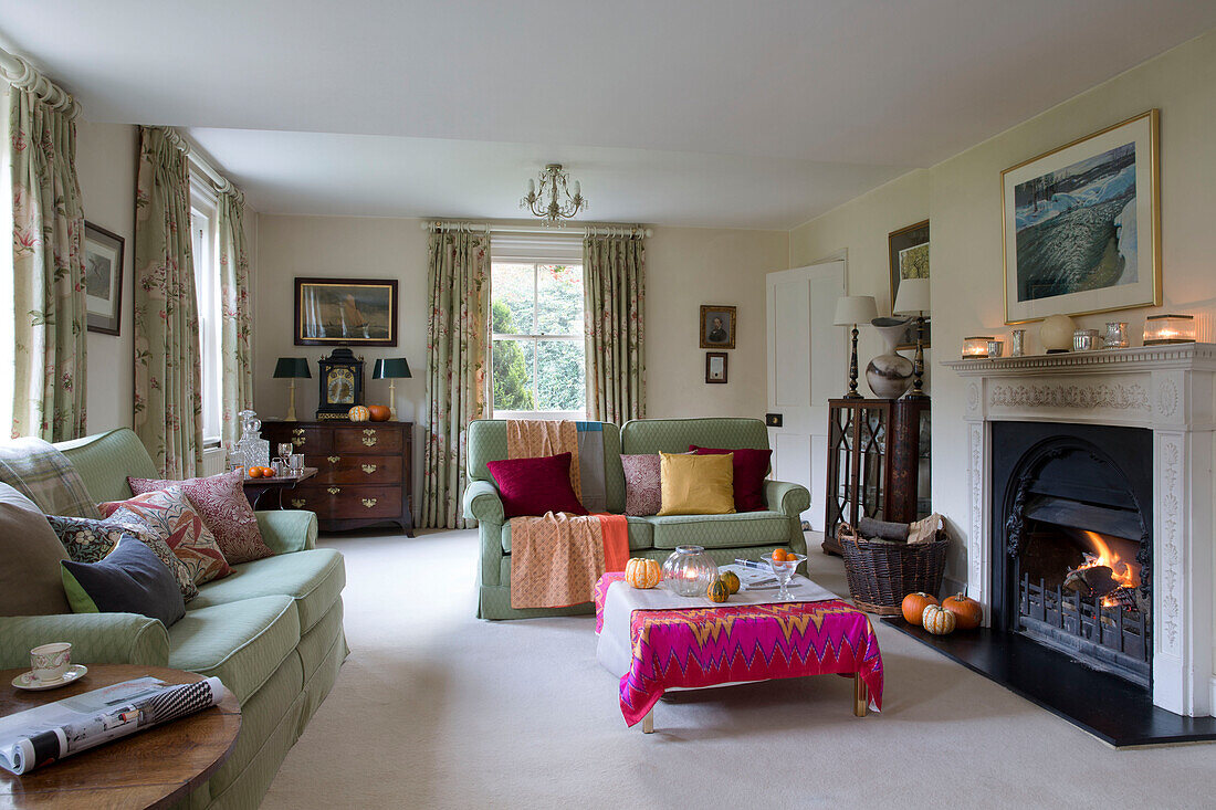 Light green sofas with low coffee table covered in pink fabric at lit fireside in London home,  England,  UK