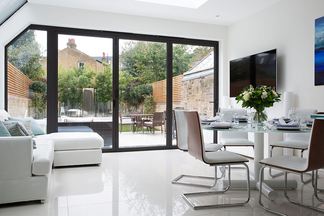 Offenes Wohnzimmer mit weißen Ledermöbeln und Blick durch Terrassentüren in den Garten eines Londoner Hauses UK