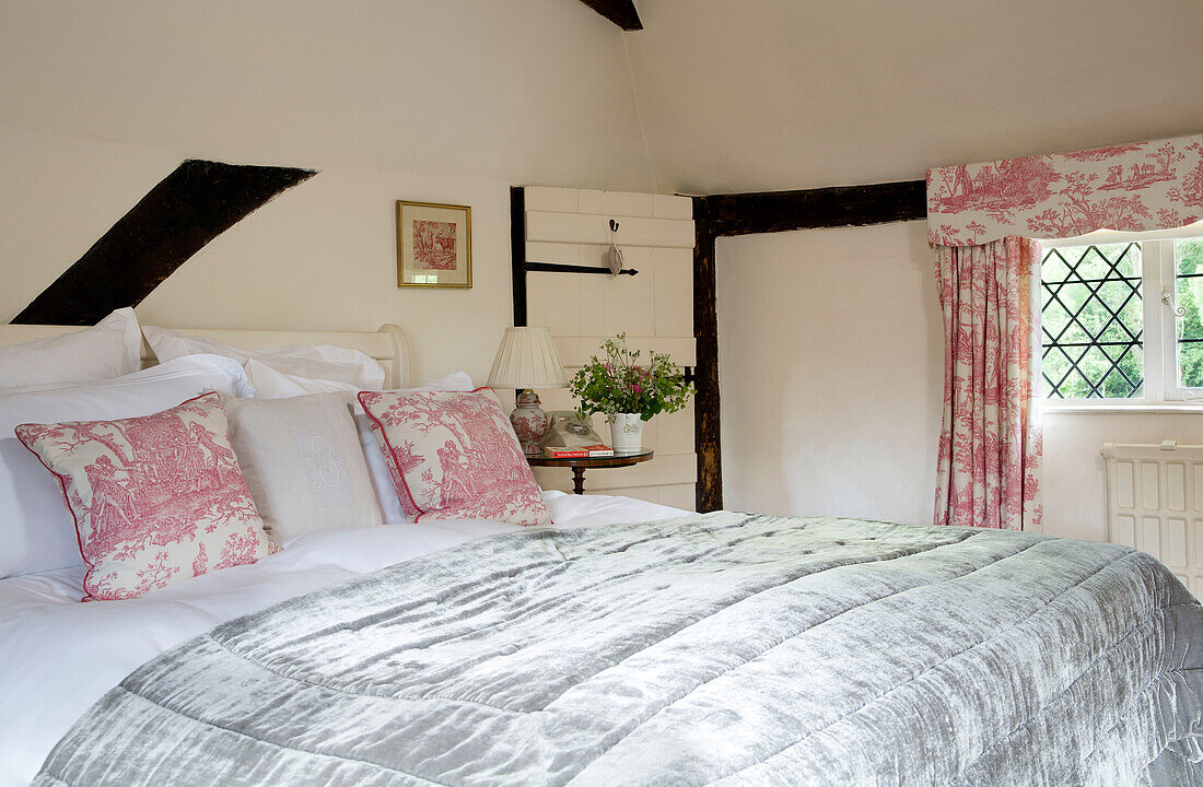 Toile de jouy curtain and cushion fabric in timber-framed bedroom of UK farmhouse