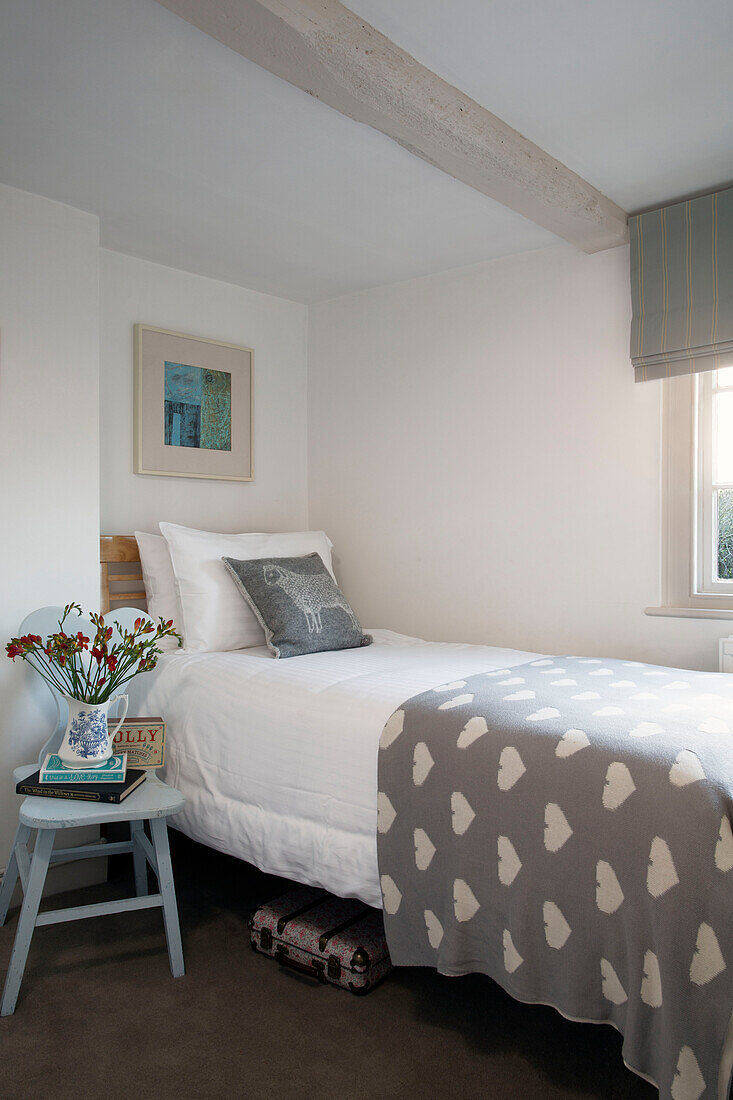 Grauer Bettbezug mit Herzmuster auf Einzelbett mit Schnittblumen auf Stuhl am Bett in Londoner Wohnung, England, UK