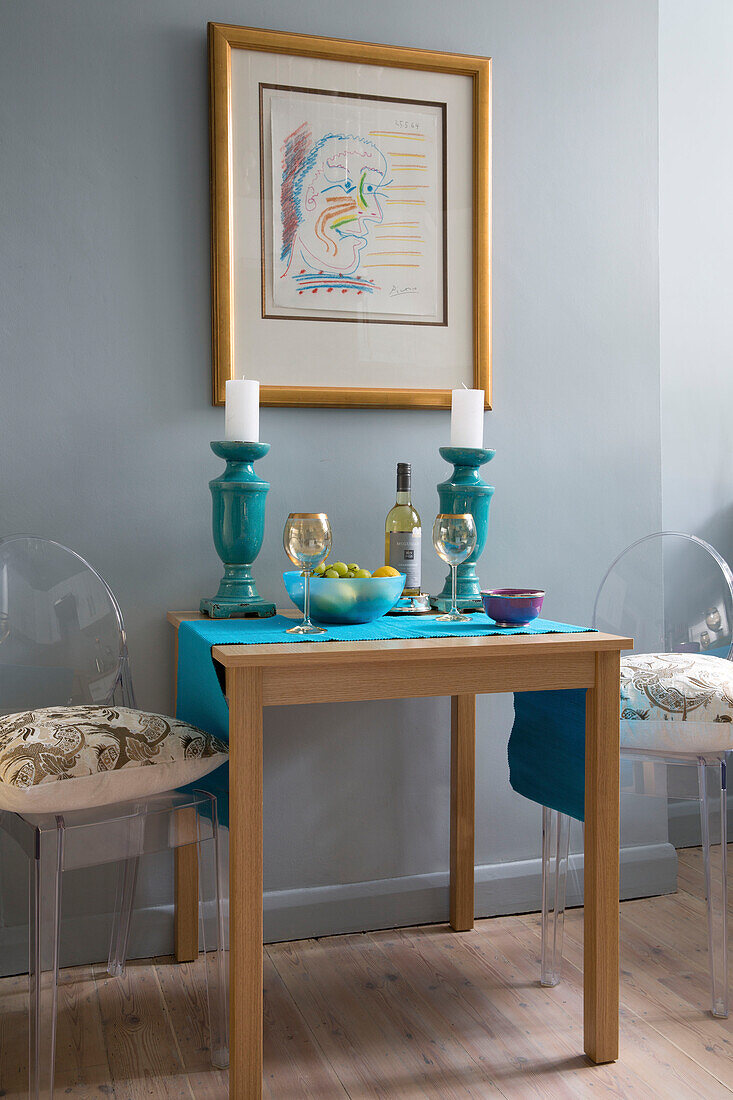 Ghost chairs at table with turquoise candle holders and framed artwork in London kitchen,  England,  UK