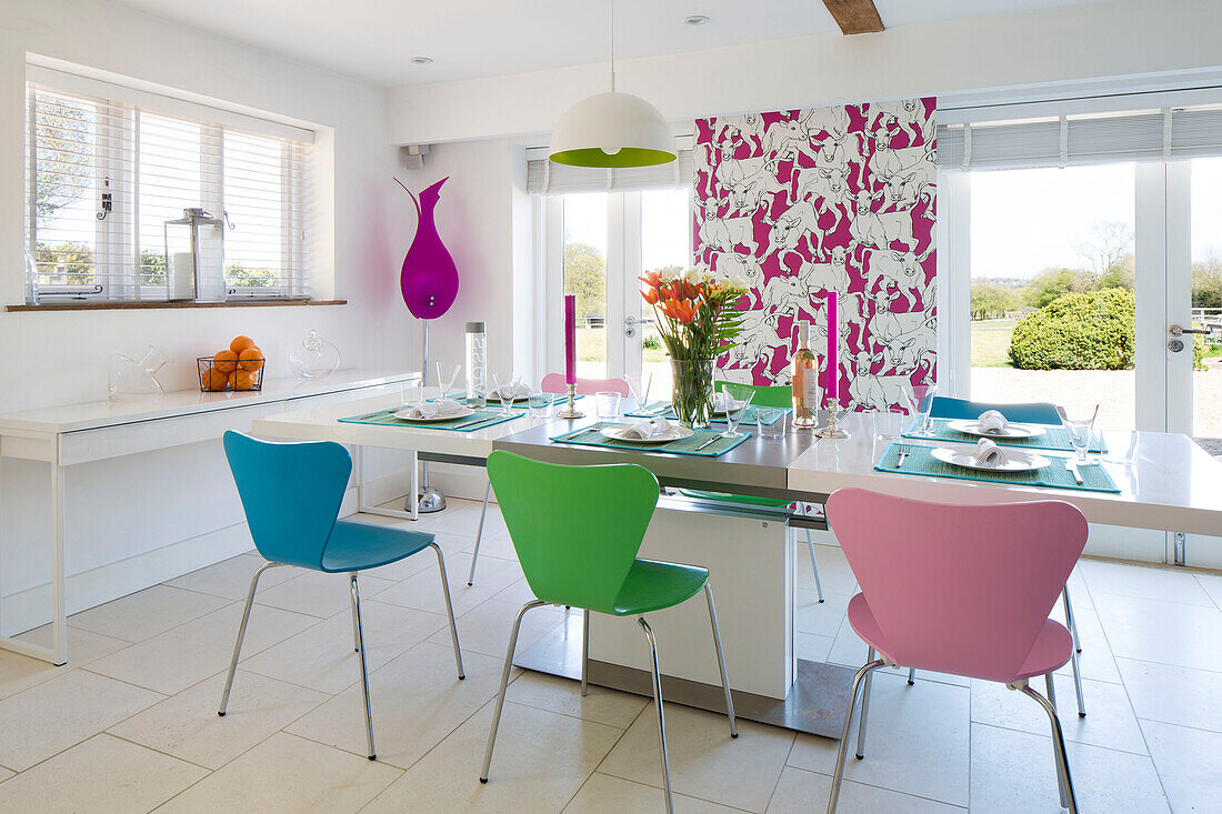 Multicoloured chairs at kitchen table with feature wall and view to garden in Sandhurst country house  Kent  England  UK